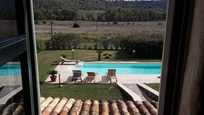 Vista desde una ventana de una zona de piscina con sillas de descanso y techo de azulejos.