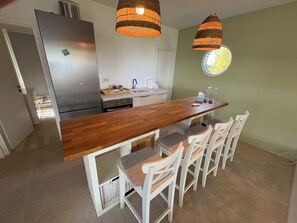 Una cocina con una isla de madera, sillas blancas y lámparas colgantes.