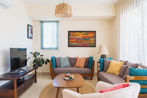 A modern living room with a sofa, armchair, coffee table, TV, and artwork.