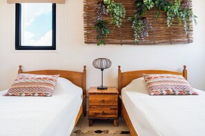 A bedroom with two wooden beds, a bedside table with a lamp, and a wall-mounted plant arrangement.