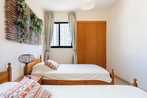 Quarto com duas camas, guarda-roupa de madeira, janela com cortinas e planta na parede.
