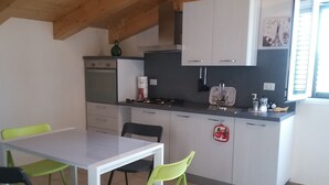 Cocina compacta con comedor, que incluye una mesa blanca, dos sillas, estufa y armarios.