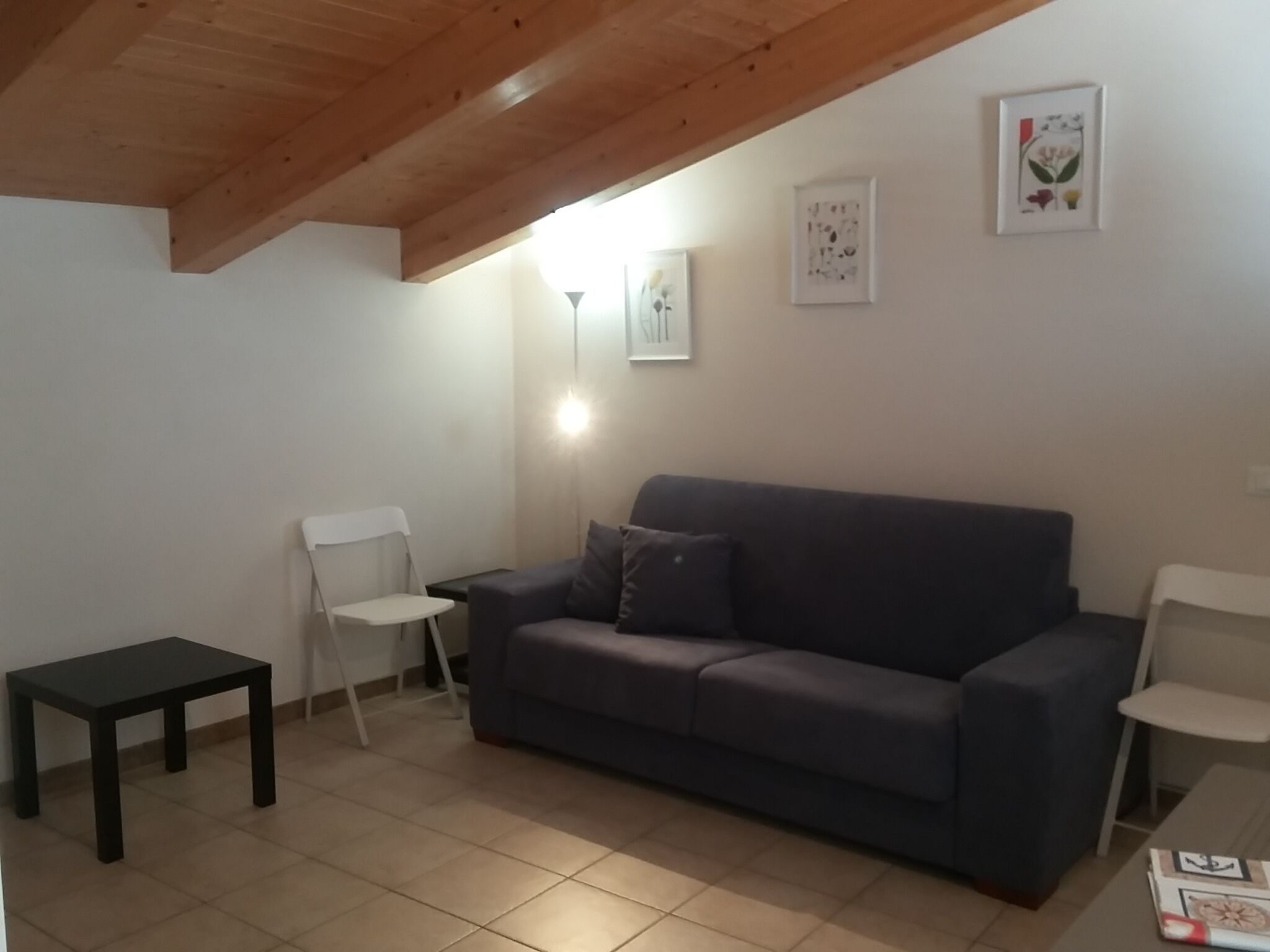 Een woonkamer met een grijze bank, een klein zwart tafeltje en een witte stoel. Twee ingekaderde foto's hangen aan de muur.