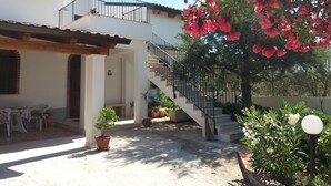 Una casa de dos pisos con un porche cubierto, una escalera y macetas con plantas.
