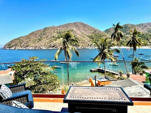 A balcony with a view of the sea, palm trees, and a mountainous landscape.