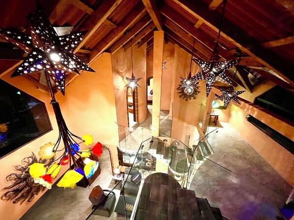 A room with a glass staircase, star-shaped hanging lights, and a wooden ceiling.