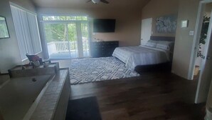 Un dormitorio con cama, ventilador de techo, ventana con persianas, televisor en la pared y baño con bañera y ducha.