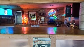 Una zona de bar con mostrador de madera, letreros de neón y varias botellas.