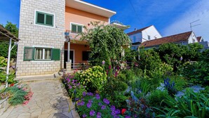 A two-story house with a stone facade, a balcony, and a garden with various plants and flowers. - Our apartment is located at quiet area, with big terrace and nice garden arround (Korčula)