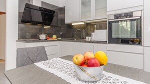 A modern kitchen with white cabinets, a black range hood, and a built-in oven. - Our apartment is located at quiet area, with big terrace and nice garden arround (Korčula)