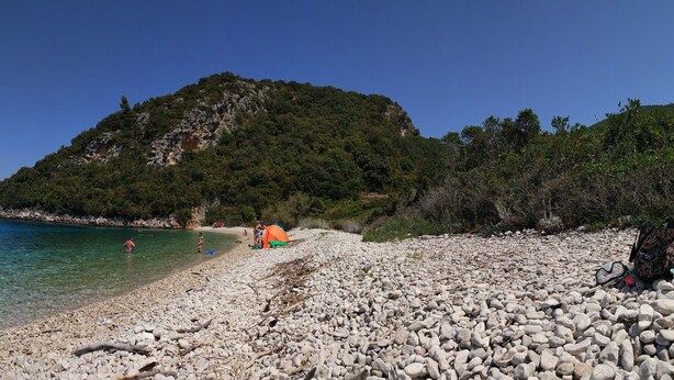 A pebble beach with clear water, a boat, and a tent. - Our apartment is located at quiet area, with big terrace and nice garden arround (Korčula)