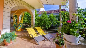 A covered patio with two yellow lounge chairs, a hammock, and potted plants. - Our apartment is located at quiet area, with big terrace and nice garden arround (Korčula)