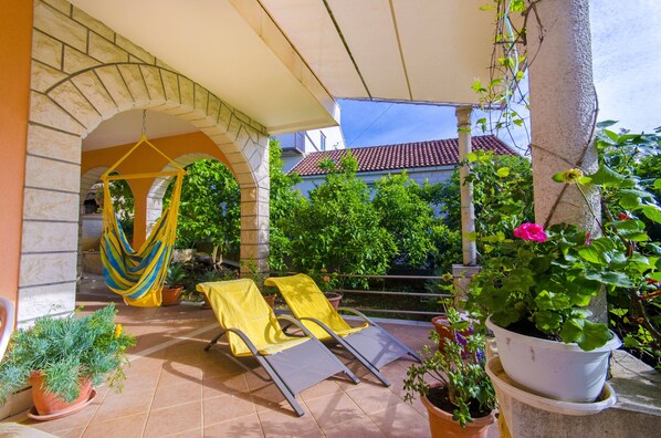 A covered patio with two yellow lounge chairs, a hammock, and potted plants.