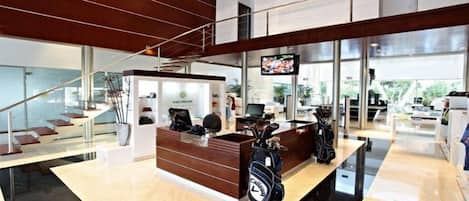 A modern hotel lobby with a reception desk, a staircase, and a large TV screen.
