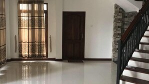 Un pasillo espacioso con piso pulido, una puerta de madera y una escalera con barandilla oscura.