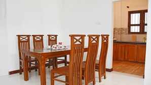 Un comedor con mesa y sillas de madera, una cocina al fondo y suelo de baldosas.