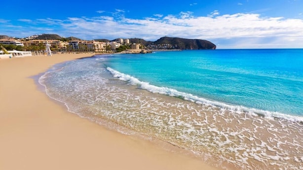 A beach with clear turquoise water, sandy shore, and buildings in the background. - See view villa with pool and big garden. (MORAIRA, (ALICANTE) ESPAÑA)