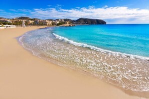 A beach with clear turquoise water, sandy shore, and buildings in the background. - See view villa with pool and big garden. (MORAIRA, (ALICANTE) ESPAÑA)