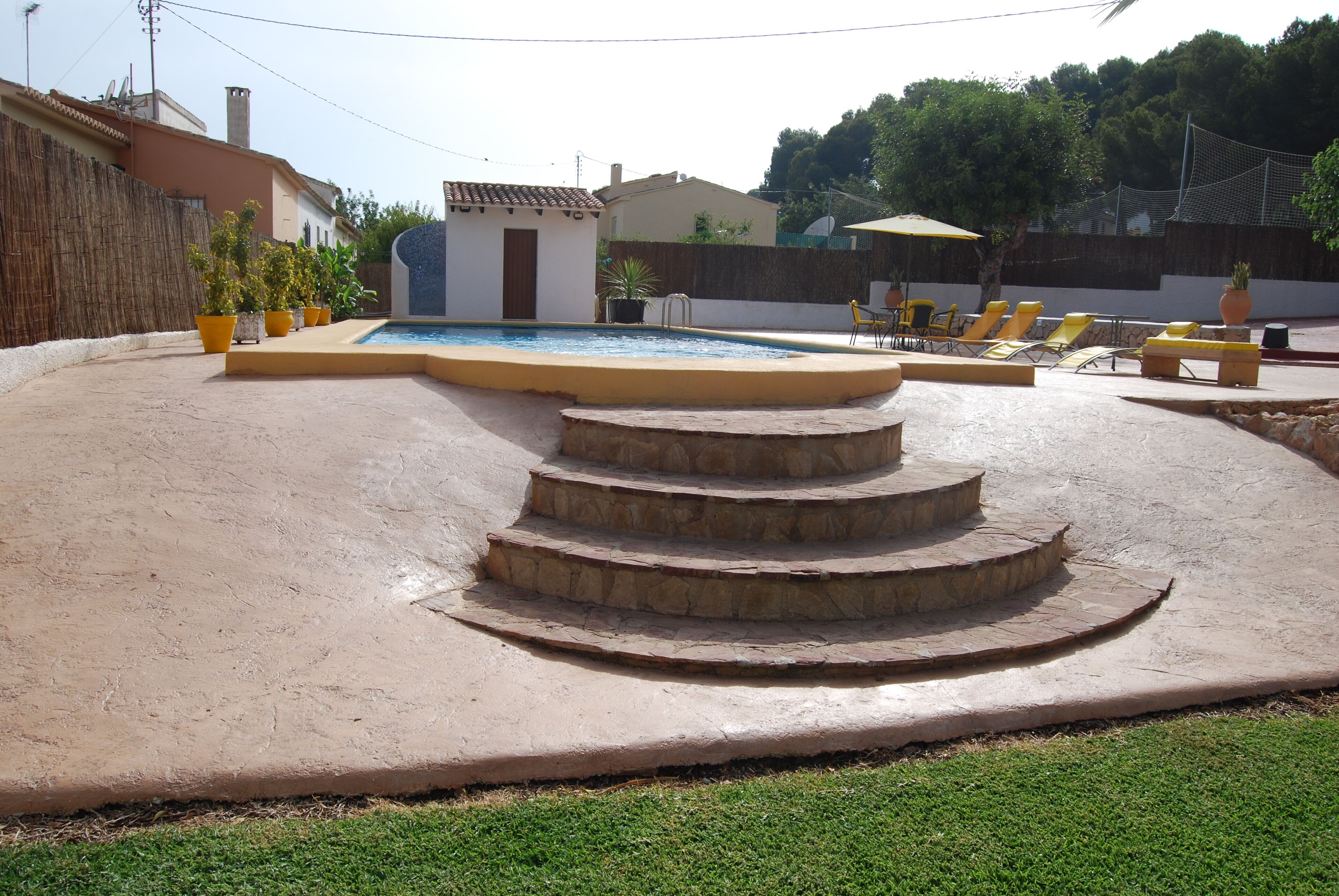 Une piscine avec un escalier en pierre menant à l’eau, entourée de chaises longues jaunes et de plantes en pot.