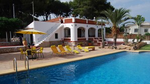 A swimming pool with yellow lounge chairs and a covered seating area with a table and chairs. - See view villa with pool and big garden. (MORAIRA, (ALICANTE) ESPAÑA)