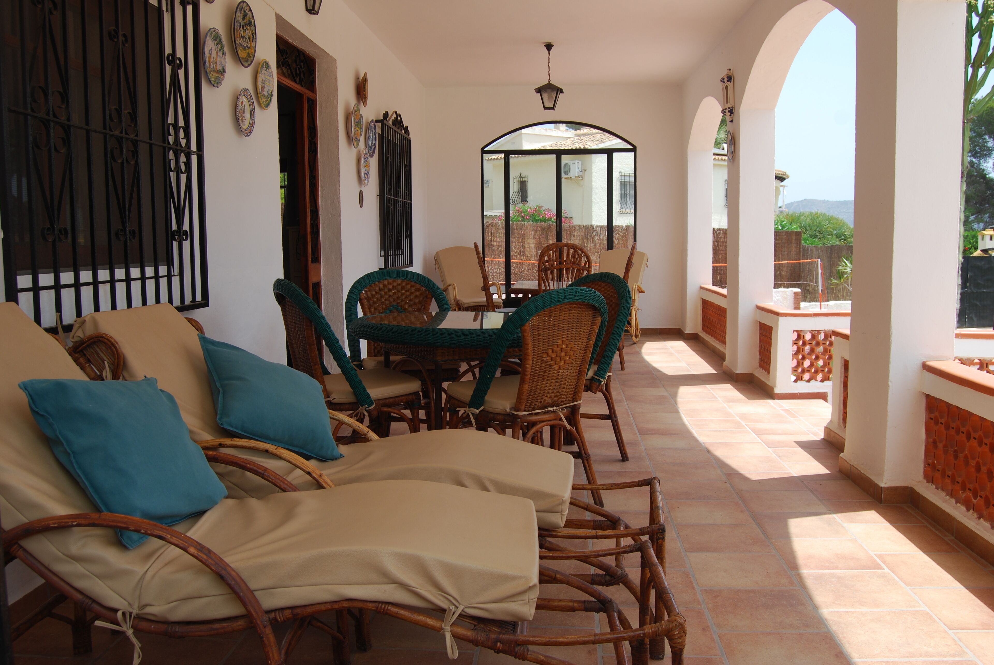 A sunlit patio with wicker furniture, a glass table, and a view of the garden.