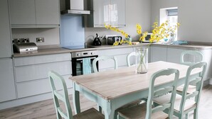 Una cocina moderna con armarios grises, una mesa de comedor de madera y sillas. Hay un jarrón con flores amarillas sobre la mesa.