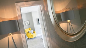 Un interior moderno con un acceso a una sala de estar que incluye un sillón amarillo y un televisor de pantalla plana.