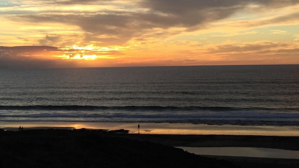 Ein Strand bei Sonnenuntergang, mit Wellen und einer Person am Ufer.