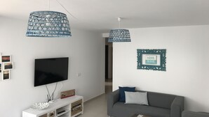 Ein modernes Wohnzimmer mit Flachbildfernseher, weißem Unterhaltungsschrank, grauem Sofa und zwei hängenden blauen Lampen.