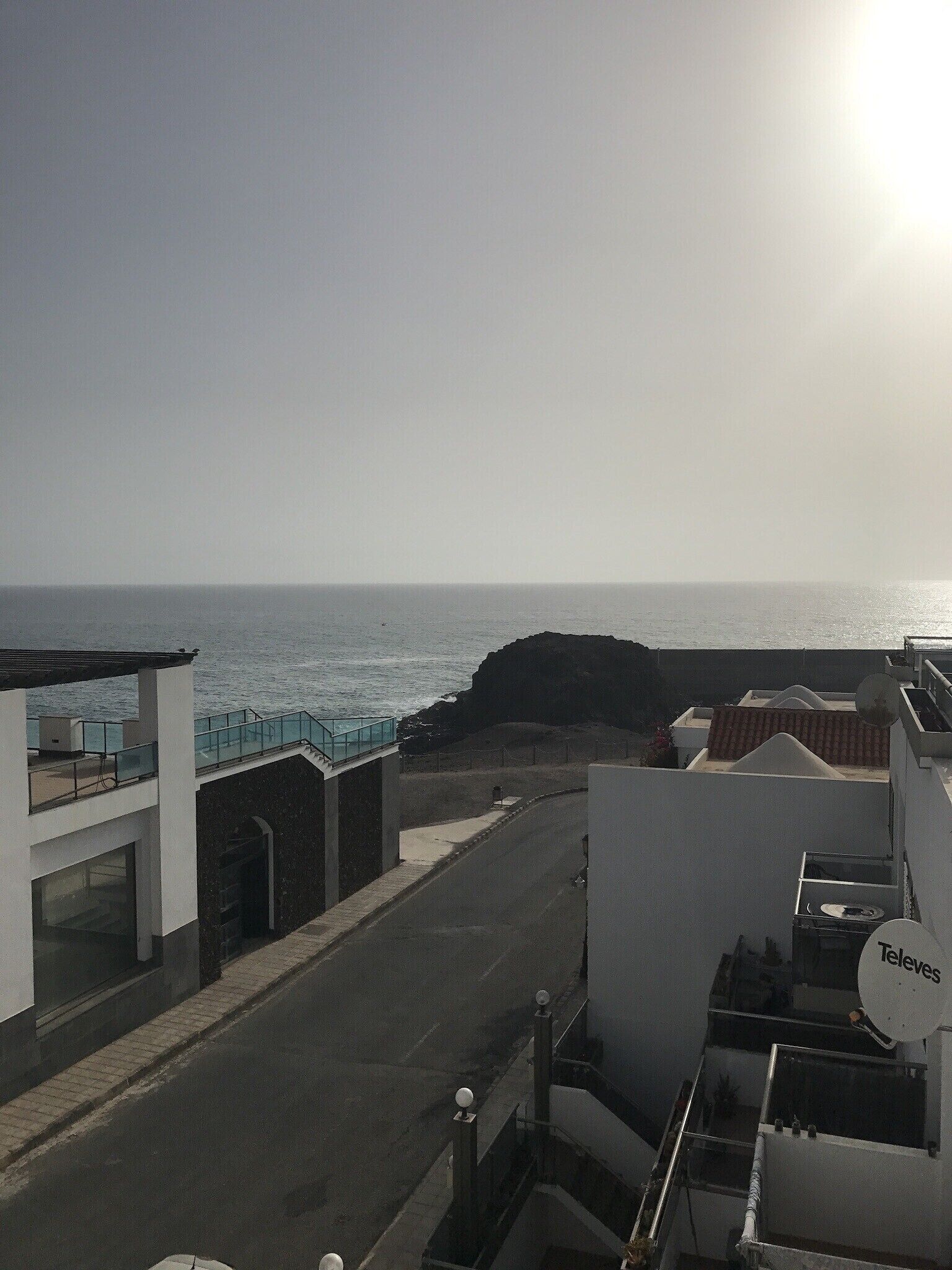 Vista sulla costa con una strada che conduce a un edificio con un'antenna satellitare con l'etichetta 'Televes'.