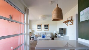 Una sala de estar moderna con un sofá, una mesa de comedor y un televisor. Hay dos cuadros en la pared, una lámpara colgante de mimbre y una pizarra verde.