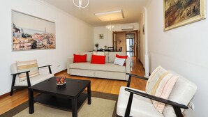 Een woonkamer met een bank, salontafel en stoelen, een schilderij aan de wand, en uitzicht op de keuken.