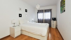 Een slaapkamer met een bed, nachtkastjes, een lamp, een televisie en een schilderij aan de muur.