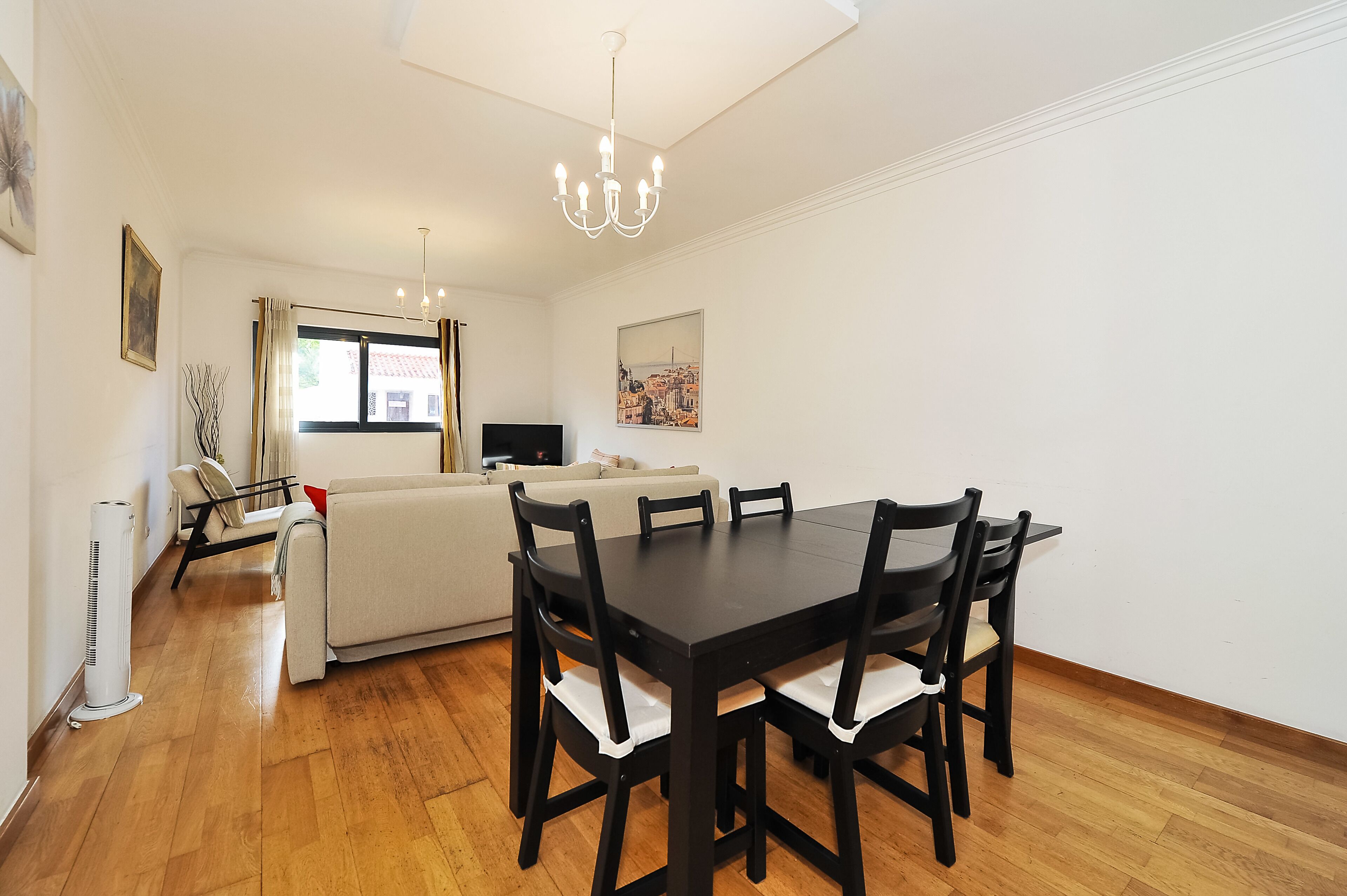 Un coin repas avec une table et des chaises noires, un canapé blanc, un téléviseur à écran plat et une fenêtre avec des rideaux.