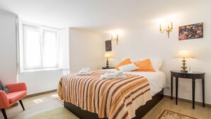 Une chambre à coucher avec un lit, deux tables de chevet, une chaise, une fenêtre et un tableau au mur.