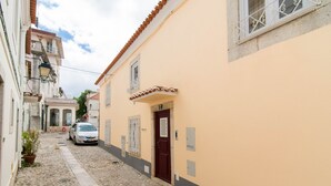 Une ruelle étroite pavée, bordée d’immeubles avec une porte rouge et une voiture garée sur le côté.