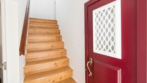 Un escalier en bois mène à une porte rouge ornée d’une fenêtre à croisillons.