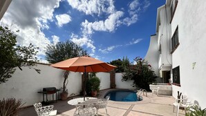 Eine Terrasse mit Pool, weißer Gartenmöbel und Kübelpflanzen.