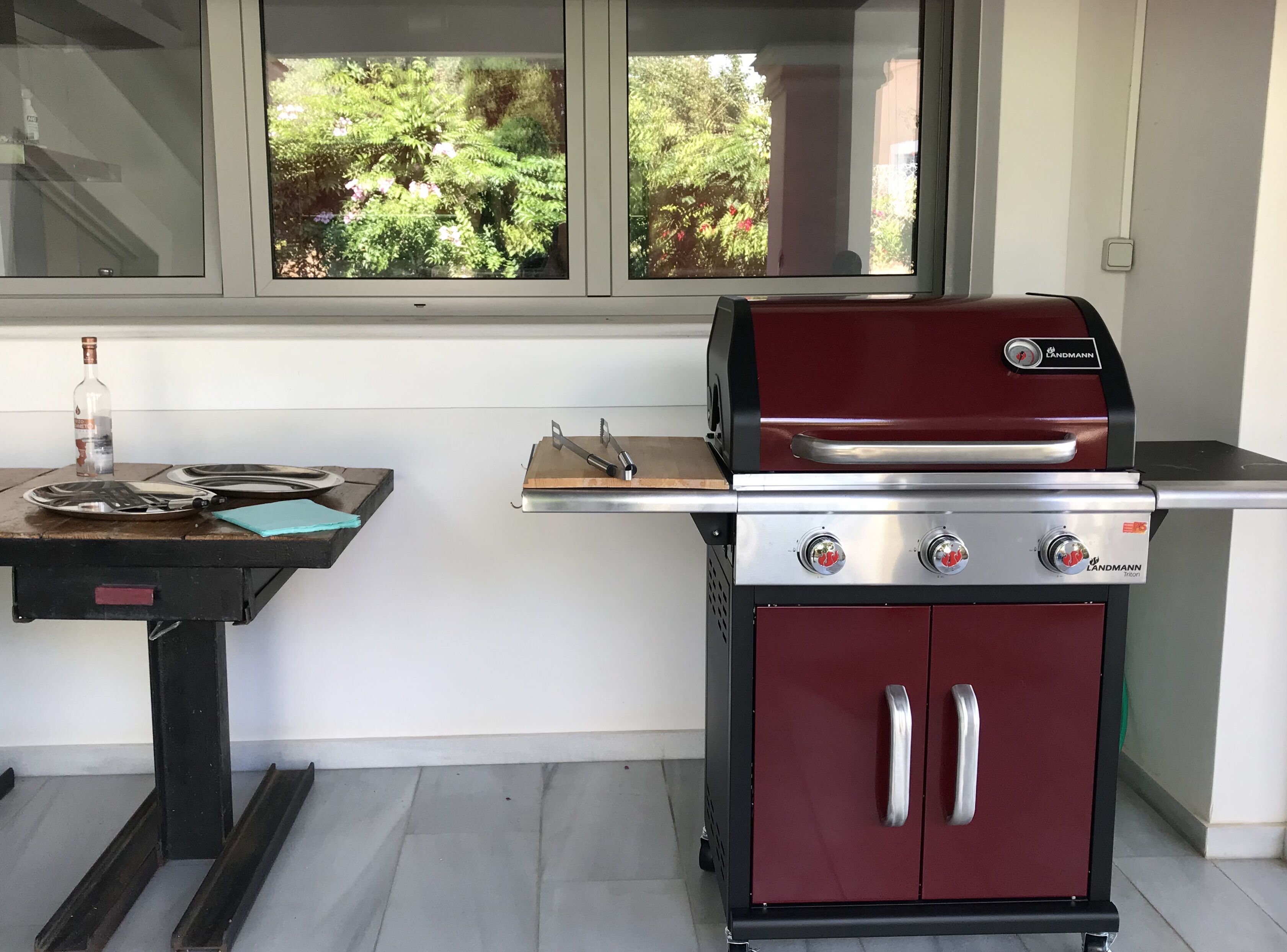 A red grill with two control knobs and a stainless steel cabinet below it.