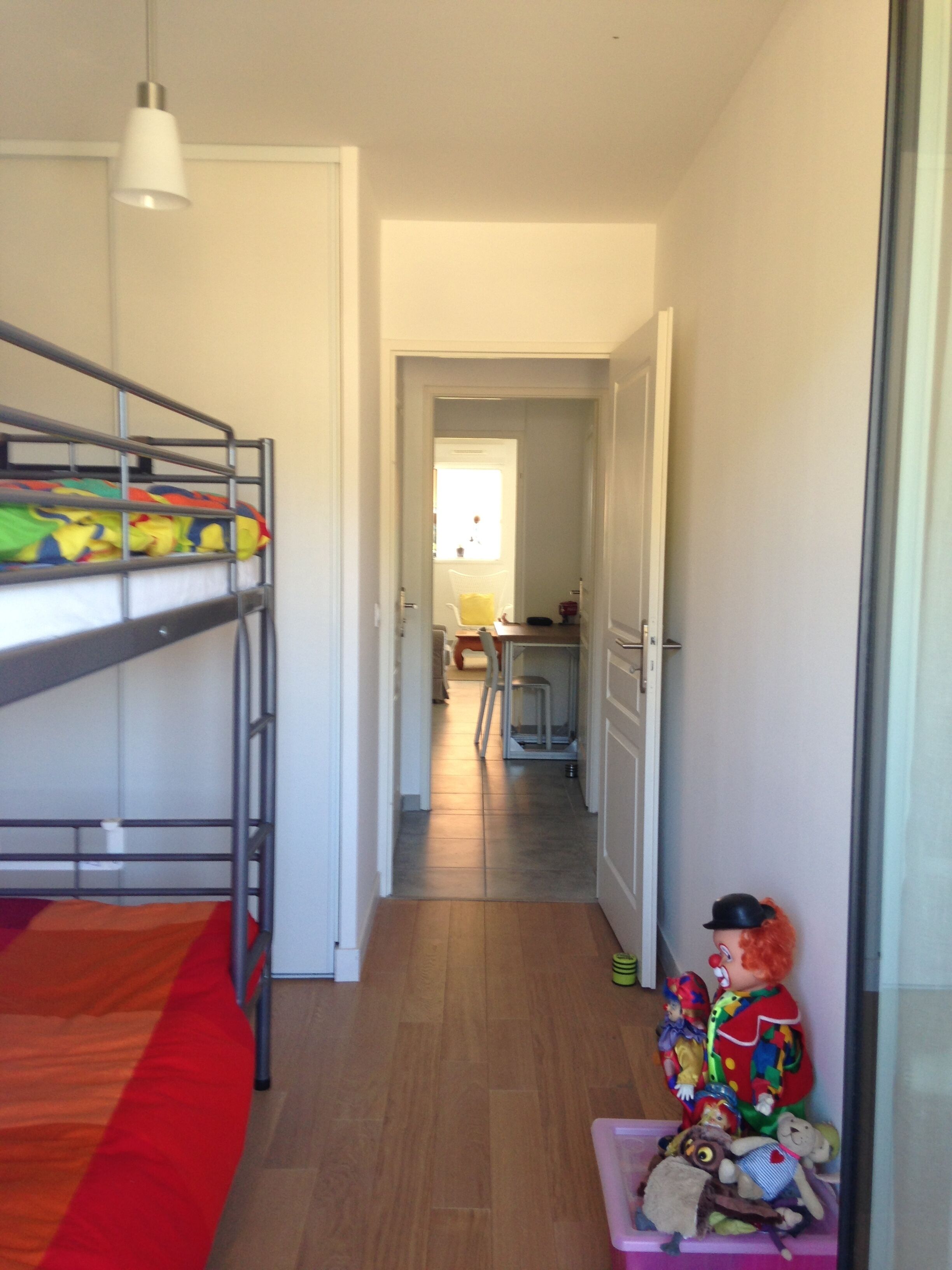 Una cama litera con ropa de cama colorida, una mesita con juguetes y una ventana con luz natural.