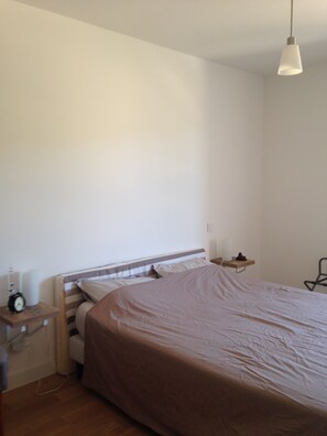 Quarto simples e arejado com uma cama de casal, mesas de cabeceira e um lustre.