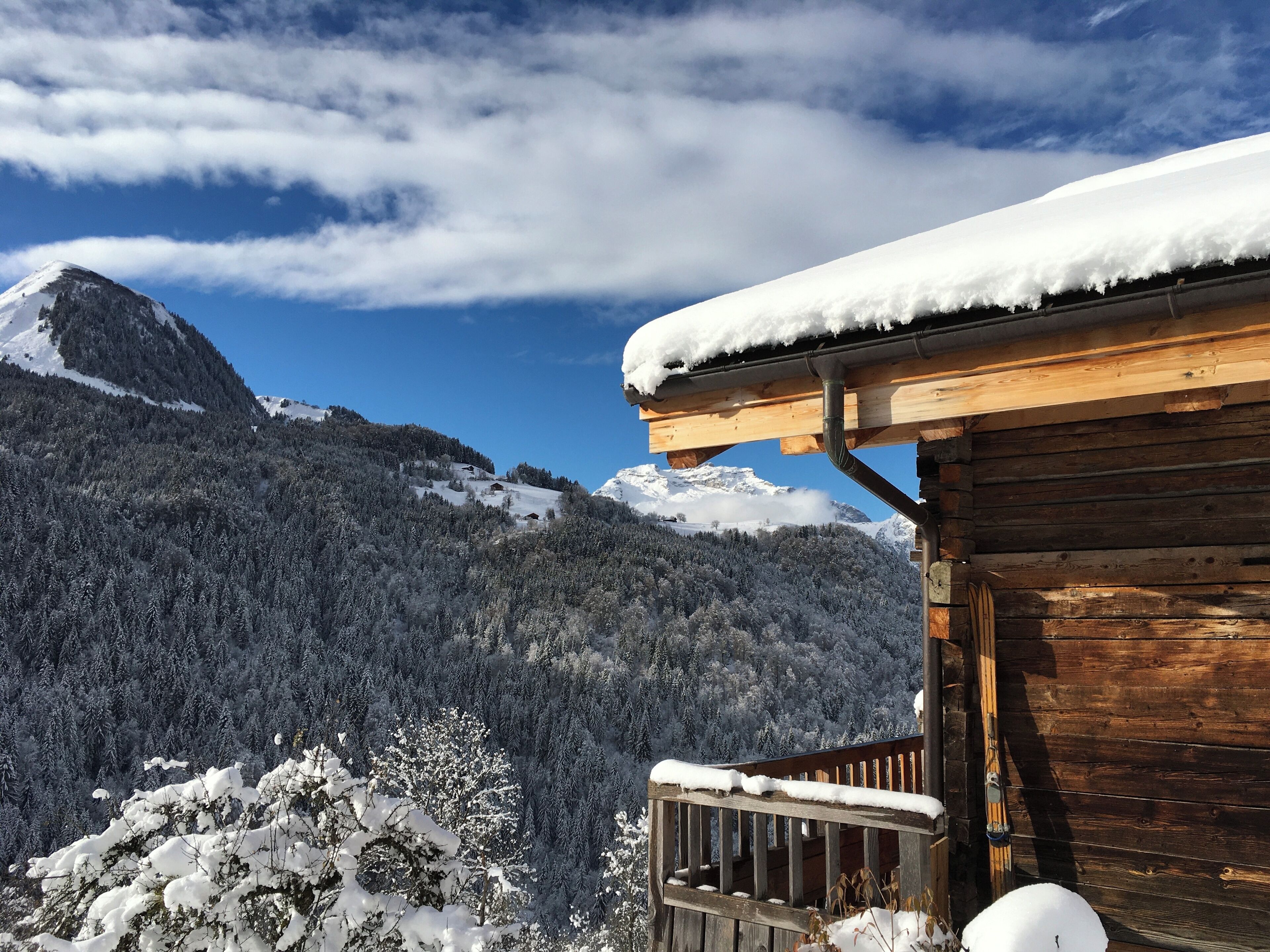Una cabaña de madera con techo nevado, frente a un paisaje montañoso.
