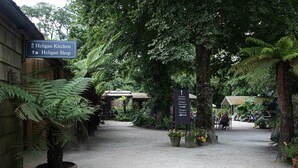 A pathway leading to a garden entrance, with signs indicating directions to Heligan Kitchen and Heligan Shop. - The Clock House at Heligan Gardens (Pentewan)