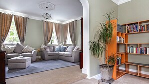 A living room with a sectional sofa, a bookshelf, and a potted plant. - The Clock House at Heligan Gardens (Pentewan)