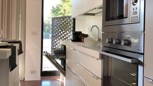 A modern kitchen with stainless steel appliances, white cabinetry, and a view of the outdoors through a sliding glass door.