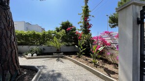 Un'area giardino con vialetti in ghiaia, diverse piante e una struttura in cemento.