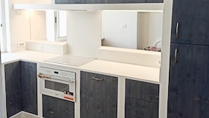 Una cucina compatta con mobili in legno scuro, ripiani in marmo bianco e un forno a incasso.