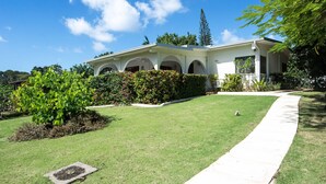 A two-story house with a covered porch, a well-maintained lawn, and a pathway leading to the entrance. - Villa Valeda on the hill (Saint James)