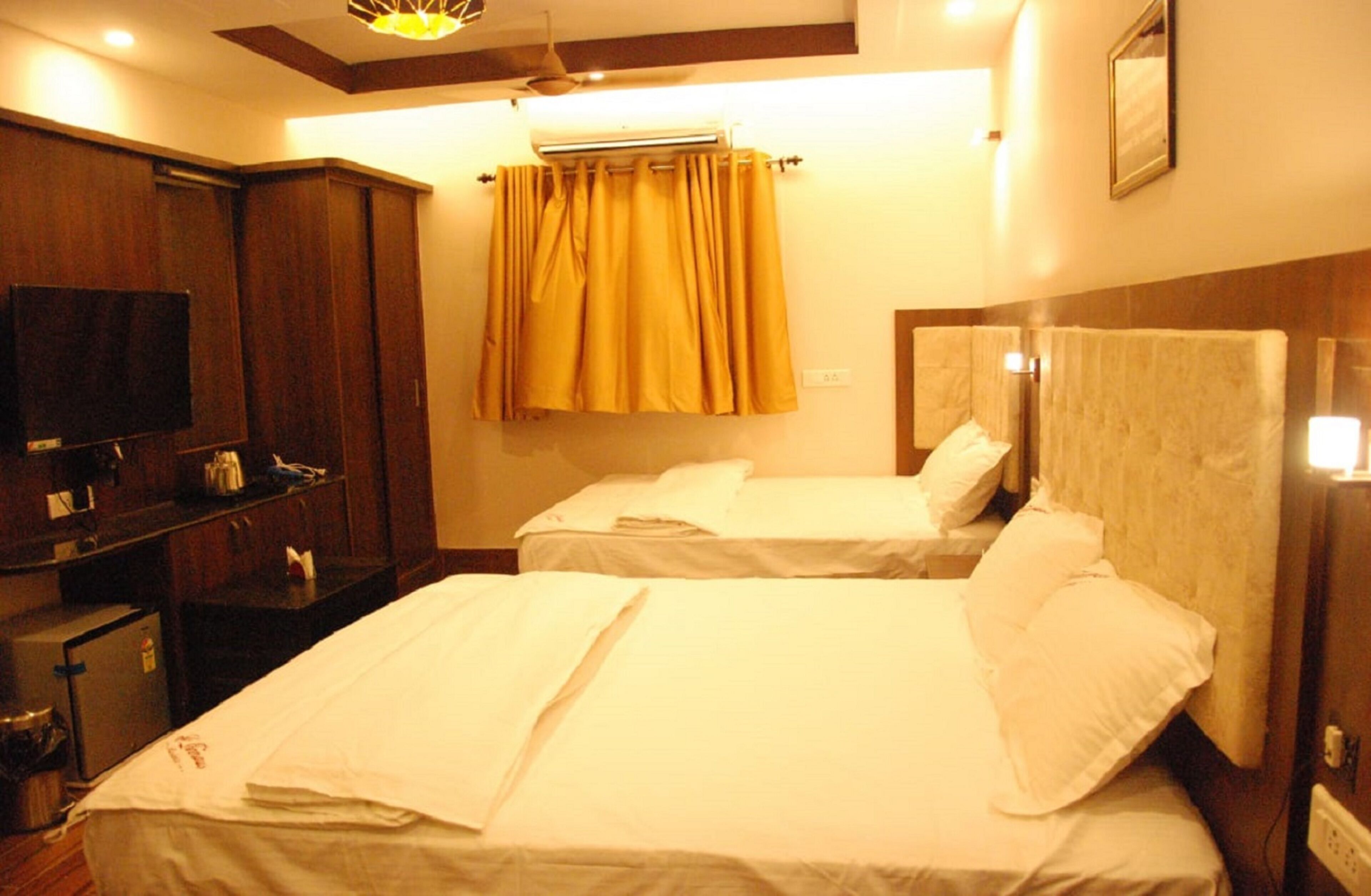 A hotel room with two beds, a TV, a small kitchenette, and an air conditioning unit.