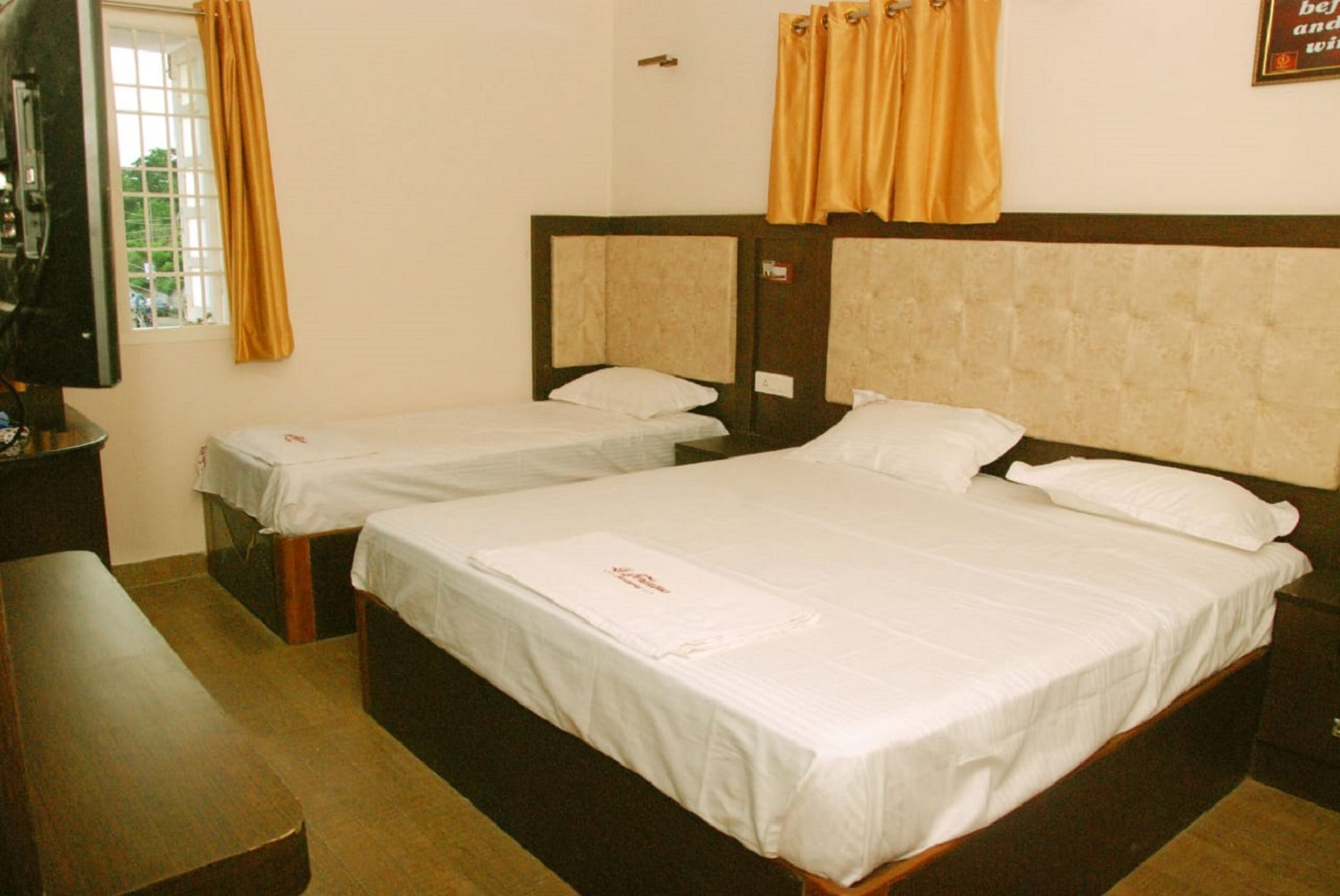 A hotel room with two single beds, a wooden bench, a television, and a window with curtains.